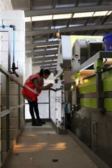 A worker in a recycling facility wearing a red safety vest examines machinery, illustrating the complexities of plastic recycling and the industry's misleading practices over decades.